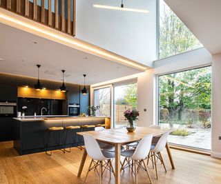 internal image of kitchen with wooden floor, large windows and doors, LED strip lighting and pendant lighting on white walls with navy kitchen to rear