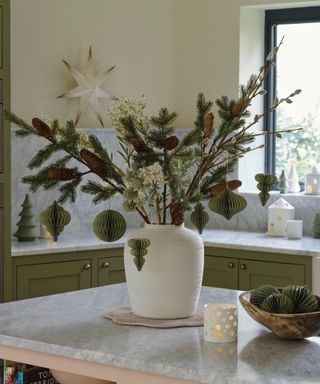 A white vase filled with Christmas tree branches decorated with paper Christmas decorations