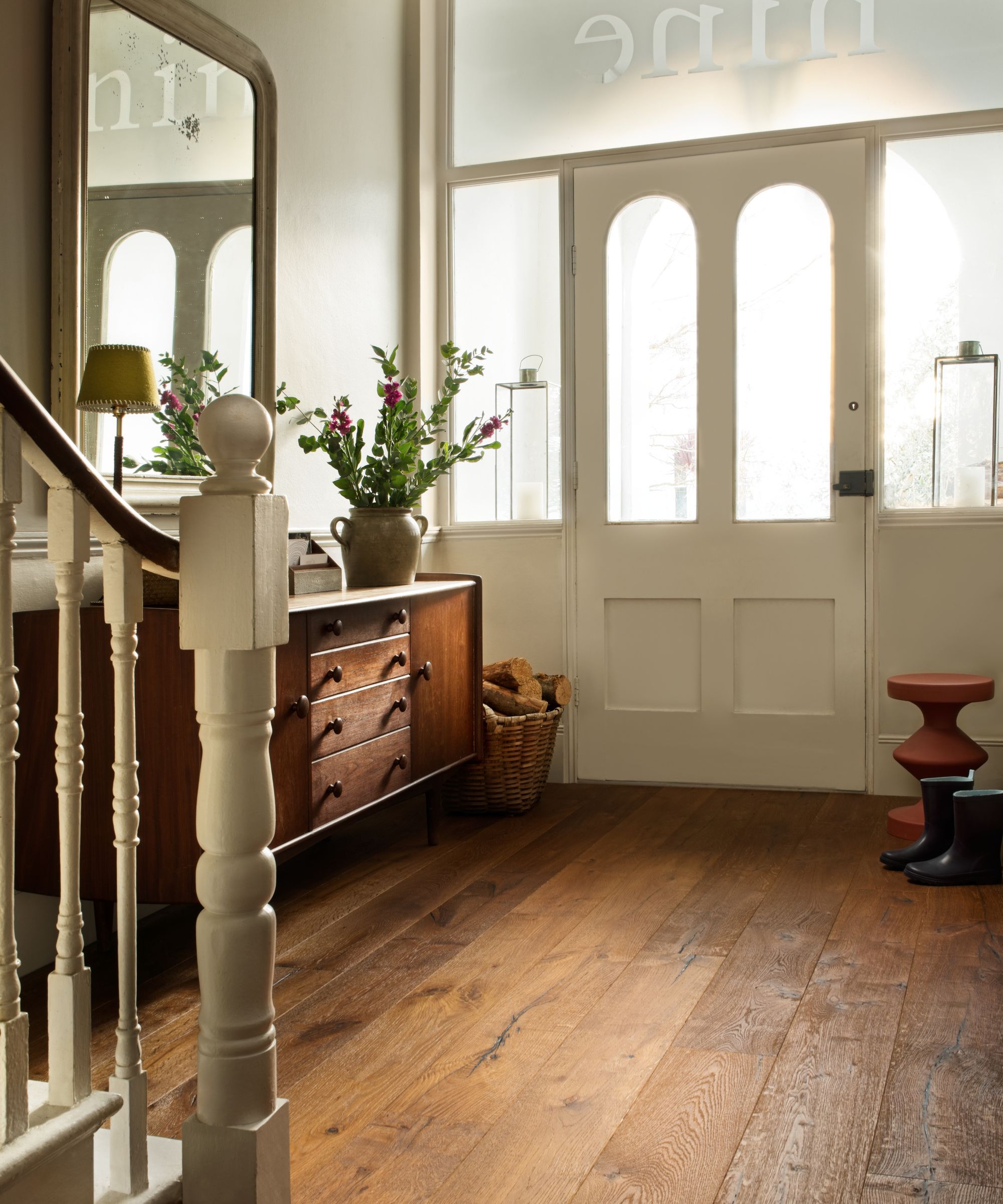 Warm and welcoming hallway featuring rich oak plank flooring, a mid-century sideboard, and soft natural light from a glazed front door with vintage charm.