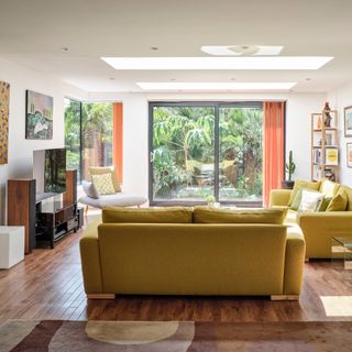 living room wood floor ideas, living room with hardwood floor, rug, two yellow sofas, chair, retro cushion, orange curtains, view to garden, tv, media unit