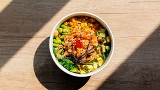 Poke bowl of healthy vegetables sitting in the sunshine on wooden counter