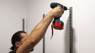 Man using a screwdriver to put up a vertical shelf bracket