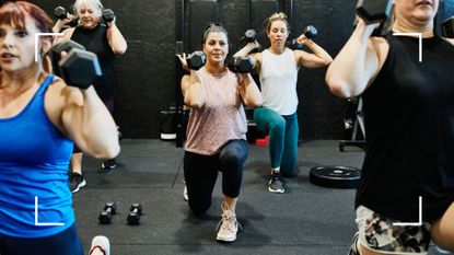 Woman holding two dumbbells in a group workout class, lunging forward, representing strength training for weight loss