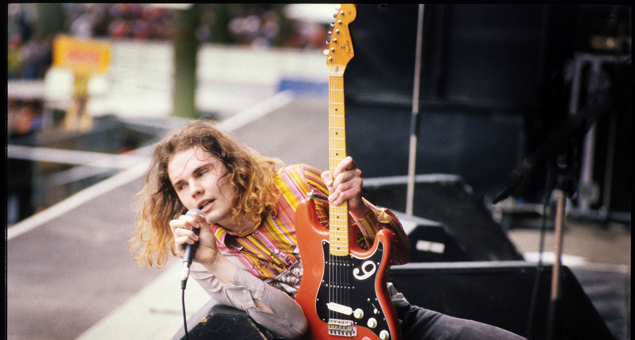 Billy Corgan of the Smashing Pumpkins with long-hair, back in 1992, lies on the stage with his orange-red Strat and sings into the mic