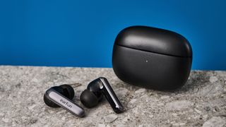 a pair of black and silver earbuds with silicone tips and a black charging case is photographed against a blue background