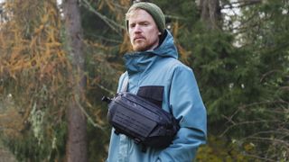 Man wearing a blue jacket outside with a Ulanzi Camera Sling Bag over his shoulder and resting on his midriff
