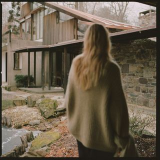 A woman with blonde hair stands outside a contemporary house
