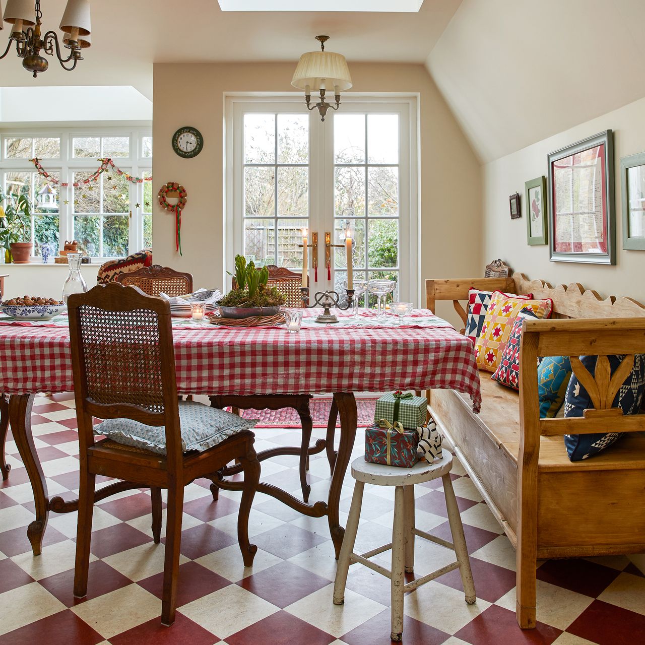dining table laid with gingham table cloth and candles, with antique chairs and bench, in front of french doors