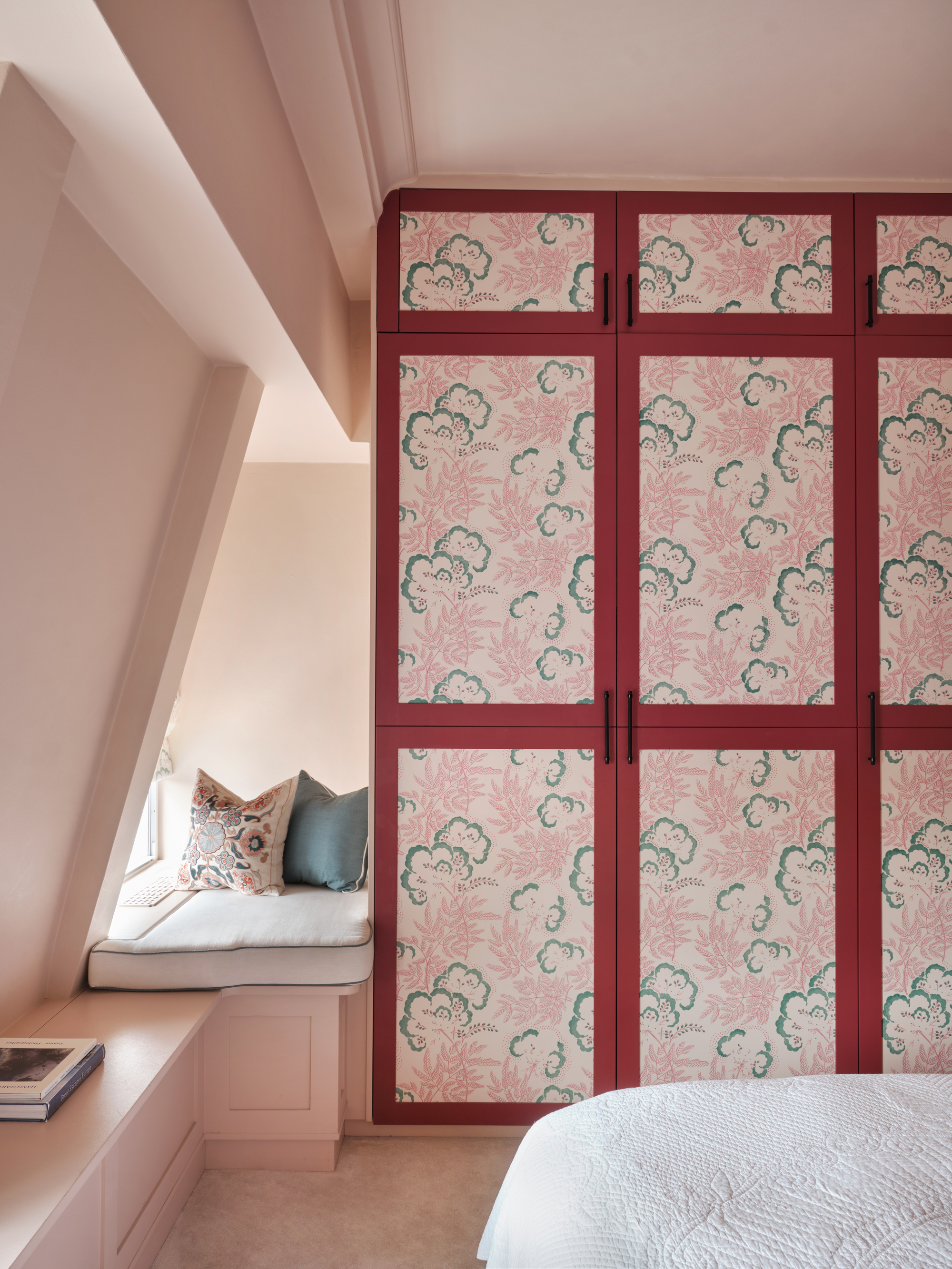 a wardrobe wrapped in wallpaper panels with pink walls, a window seat, and red trim