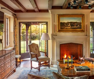living room with ceiling beams and fire lit with wainscot walls and taupe armchair and ornate wood chest