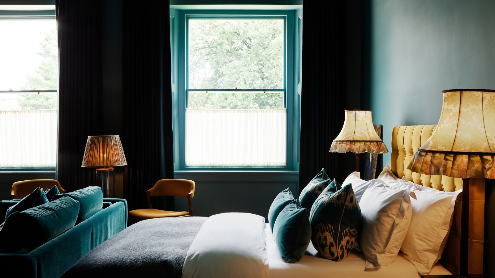A bedroom with color-drenched teal walls and a mustard bed with white and teal bedding.