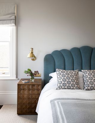 Grey bedroom with grey scallop headboard and wall lamp