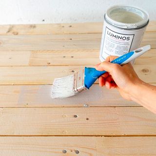 varnishing wooden pallet with painting brush and white wall