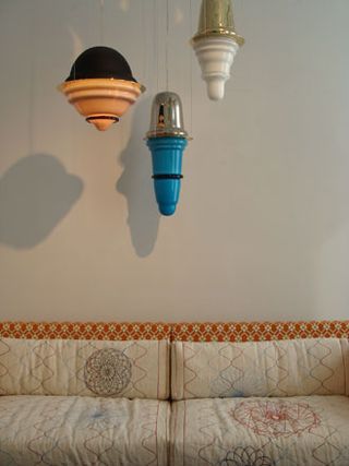 Three lamps of different colours and shapes hang above a patterned sofa