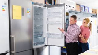 Salesman showing inside of fridge to woman in store