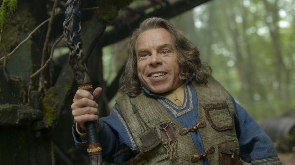 Warwich Davis&#039; Willow smiles as he greets some people standing off camera in the character&#039;s Disney Plus series