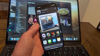 iPhone 16 in hand with MacBook Air 13-inch M3 in background showing AirDrop to laptop