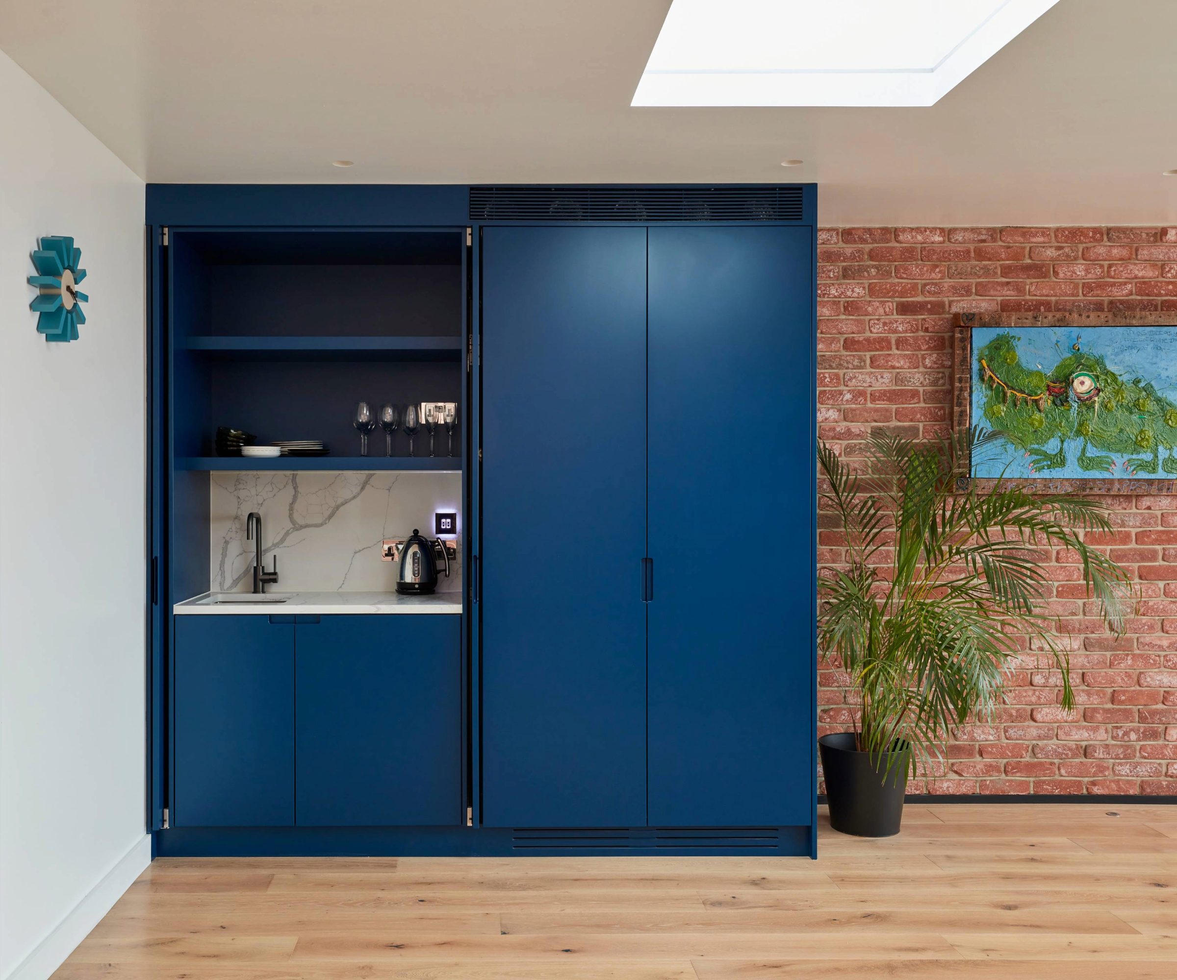 Blue kitchen unit with marble splash back next to brick wall and on wooden flooring