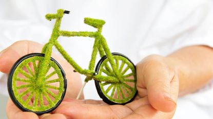 A miniature bike that looks like it's made out of grass is held in two hands