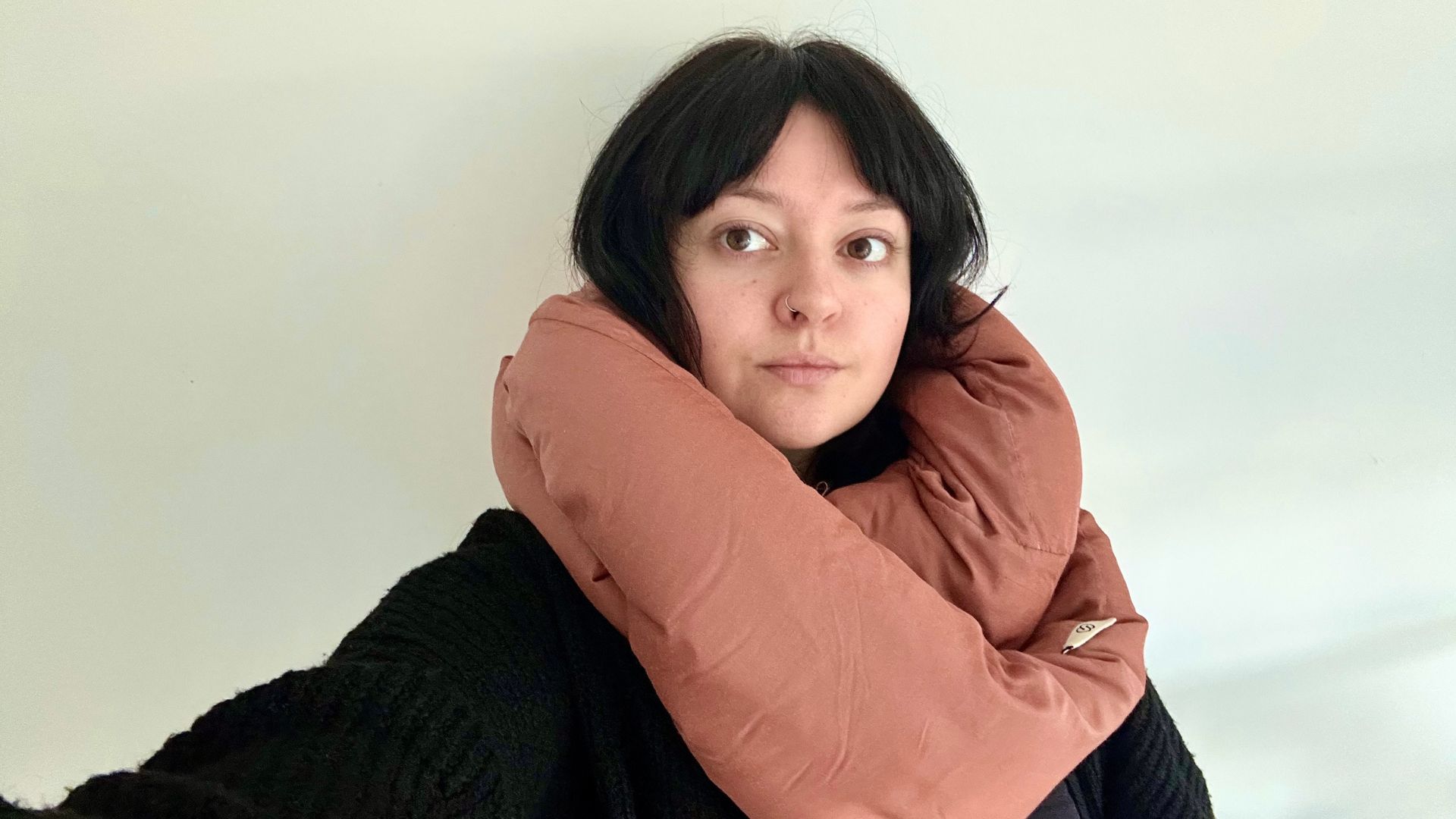 The Tom&#039;s Guide Sleep Features Editor looking at the camera with a brown Huzi Infinity Pillow wrapped around her neck