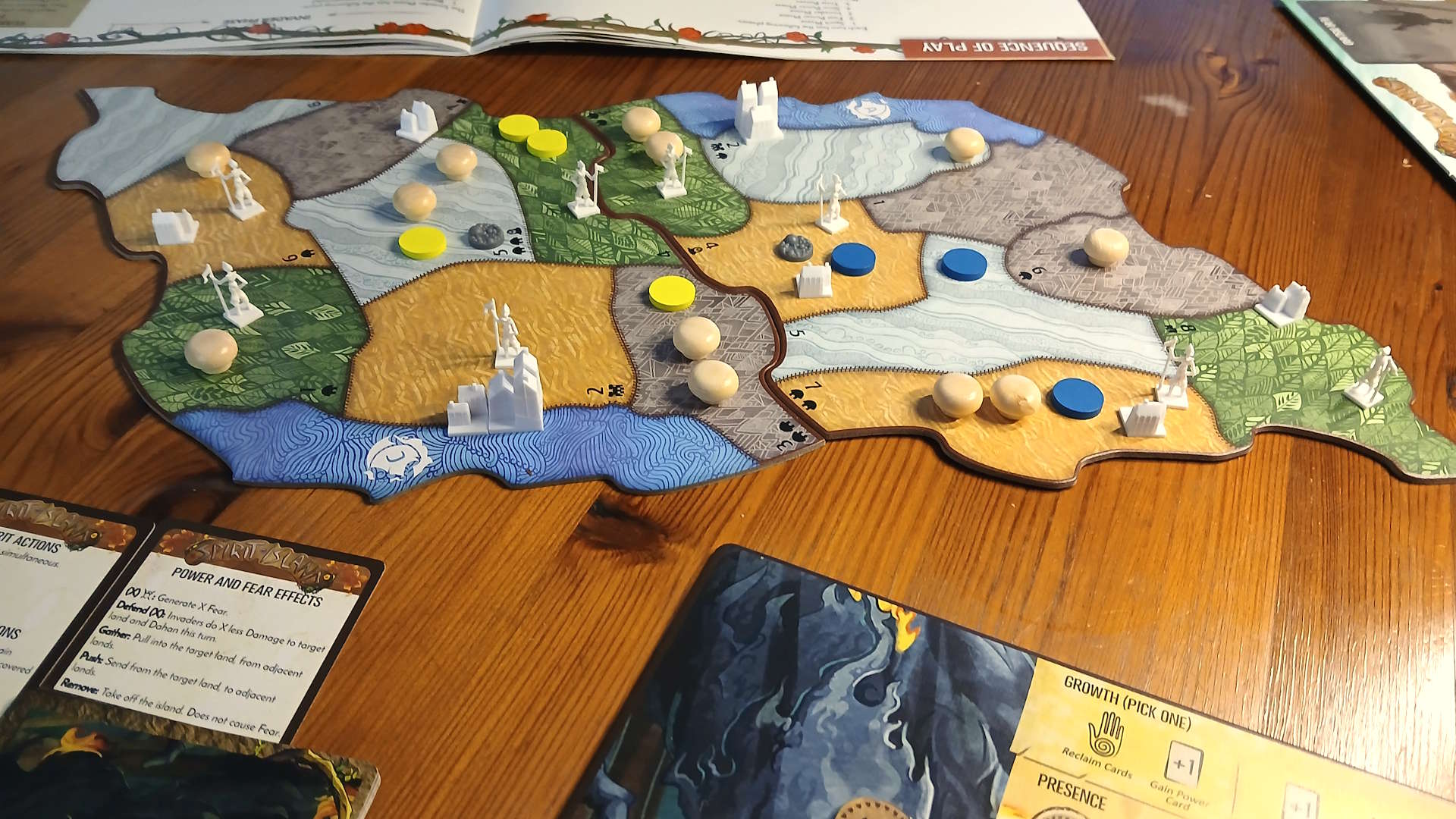 Spirit Island components, cards, and board pieces on a wooden table