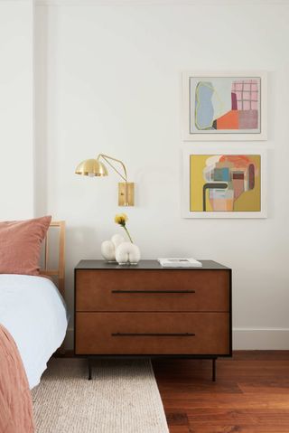 A bedroom with pastel pink linen and a gold wall sconce