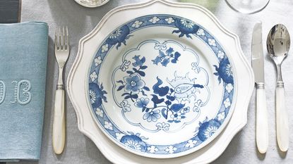 White table with pale blue napkin, white cutlery and a white charger plate with blue and white patterned crockery