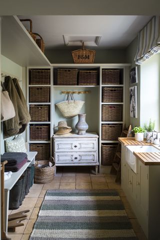 An example of mudroom ideas showing a mudroom with a striped rug, wall storage with wicker baskets, and a sink area to the right