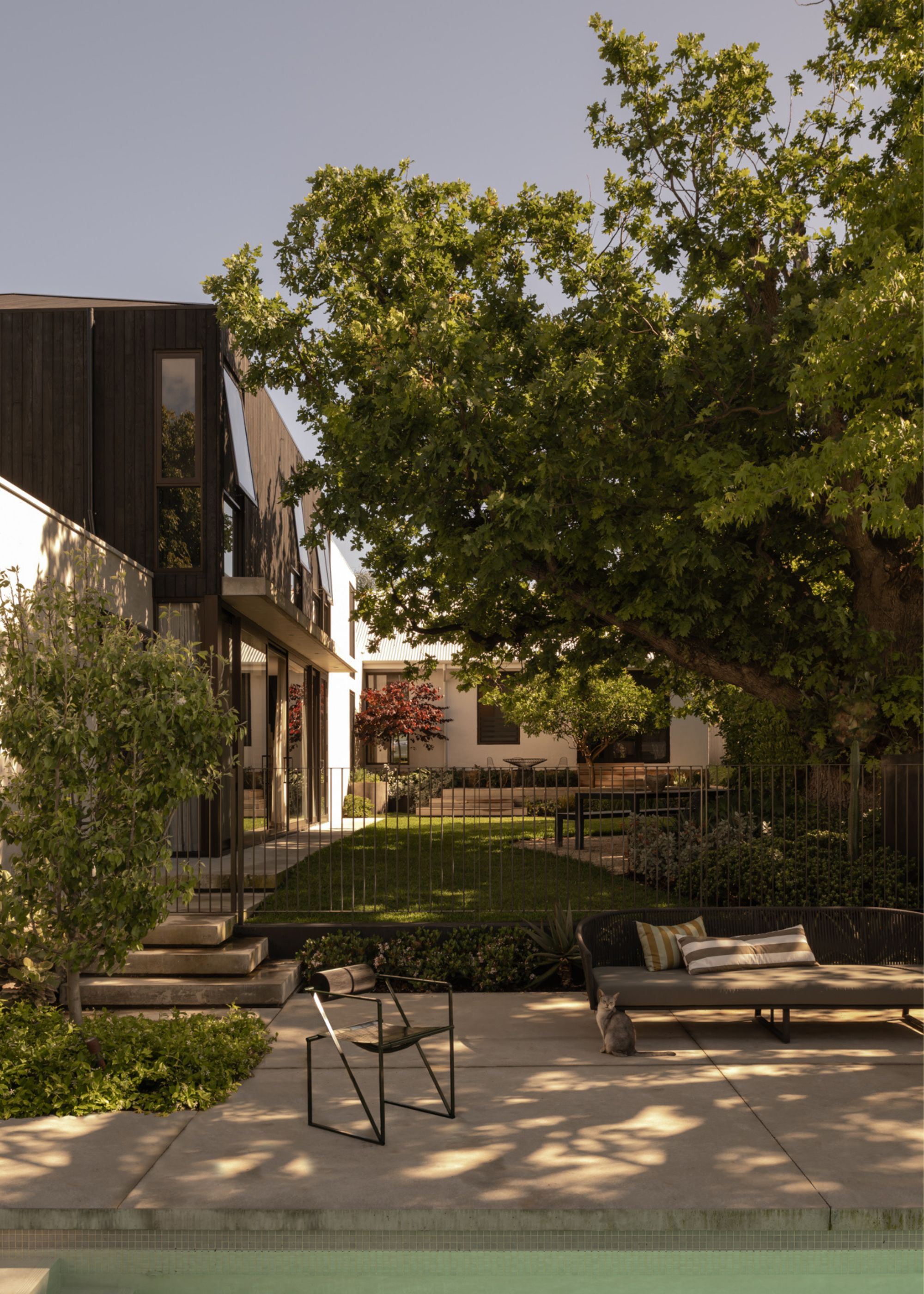 A Japanese outdoor garden with a bench, a lawn, tall trees, a metal chair, and a pool