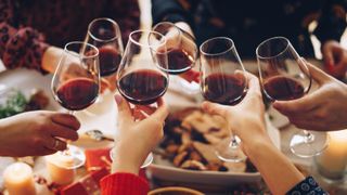 group clinking red wine glasses at dinner table