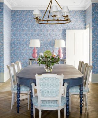 Traditional dining room with blue and white wallpaper, pink lamp shades and accents, dark wood dining table and upholstered dining chairs