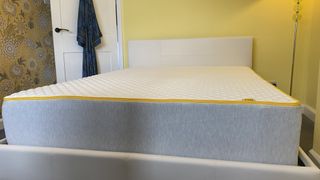 The Eve Premium Hybrid mattress photographed on our reviewer's white bed placed in a yellow bedroom