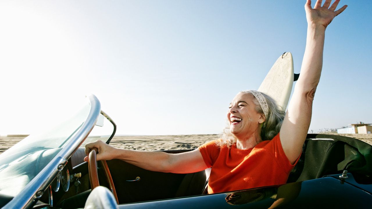 Woman arrives to beach in vintage car with surfboard in backseat.