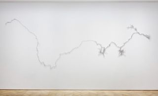 White wall, silver sculpture depicting the line of a river, wooden floor