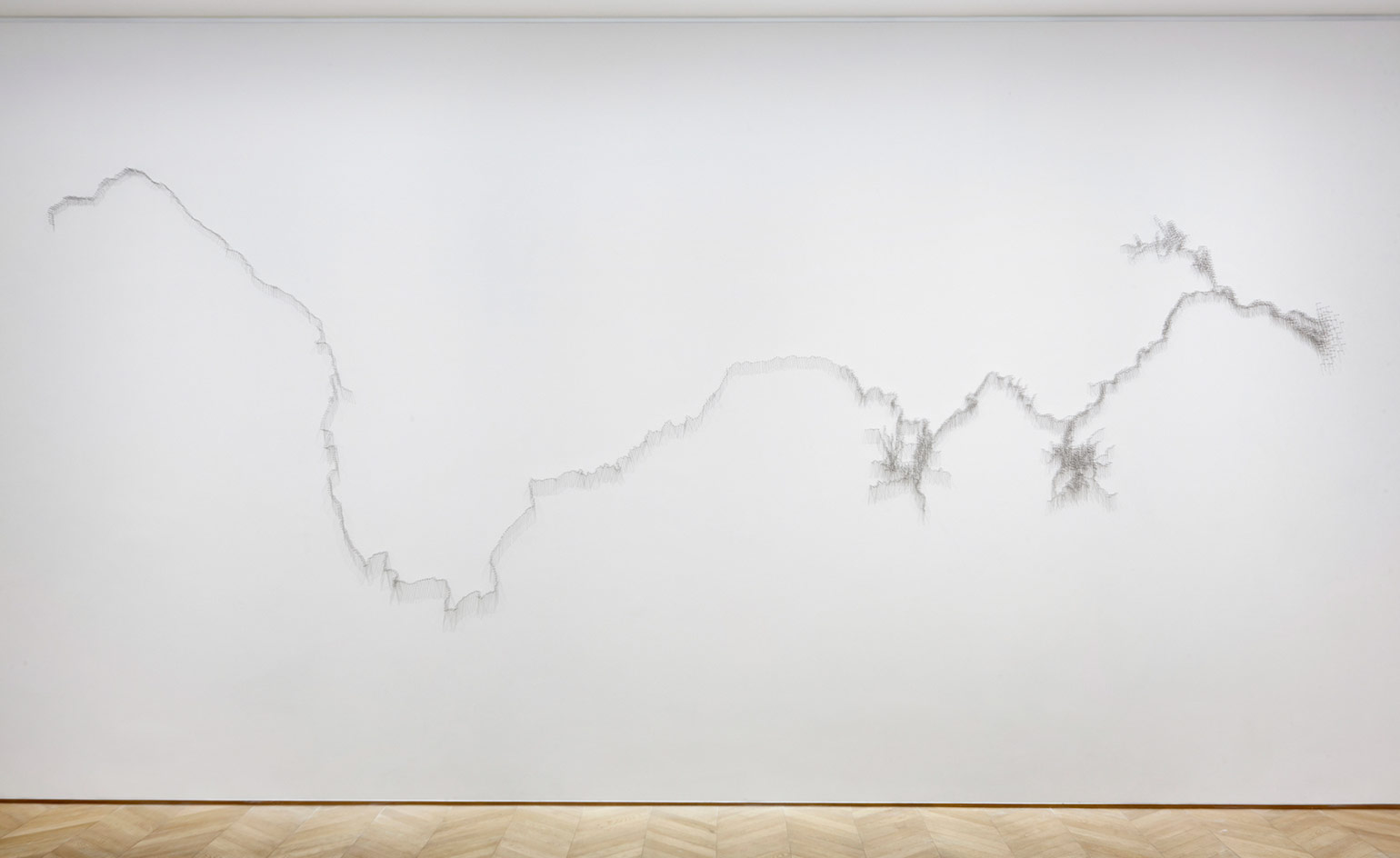 White wall, silver sculpture depicting the line of a river, wooden floor