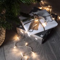 A set of white LED Christmas lights are draped across wrapped presents.