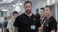 Noah Wyle walking in The Pitt with Shawn Hatosy and Ken Kirby standing behind him. 