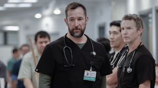 Noah Wyle walking in The Pitt with Shawn Hatosy and Ken Kirby standing behind him. 