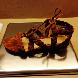 A flat woven suede sandal displayed on a silver flat stand