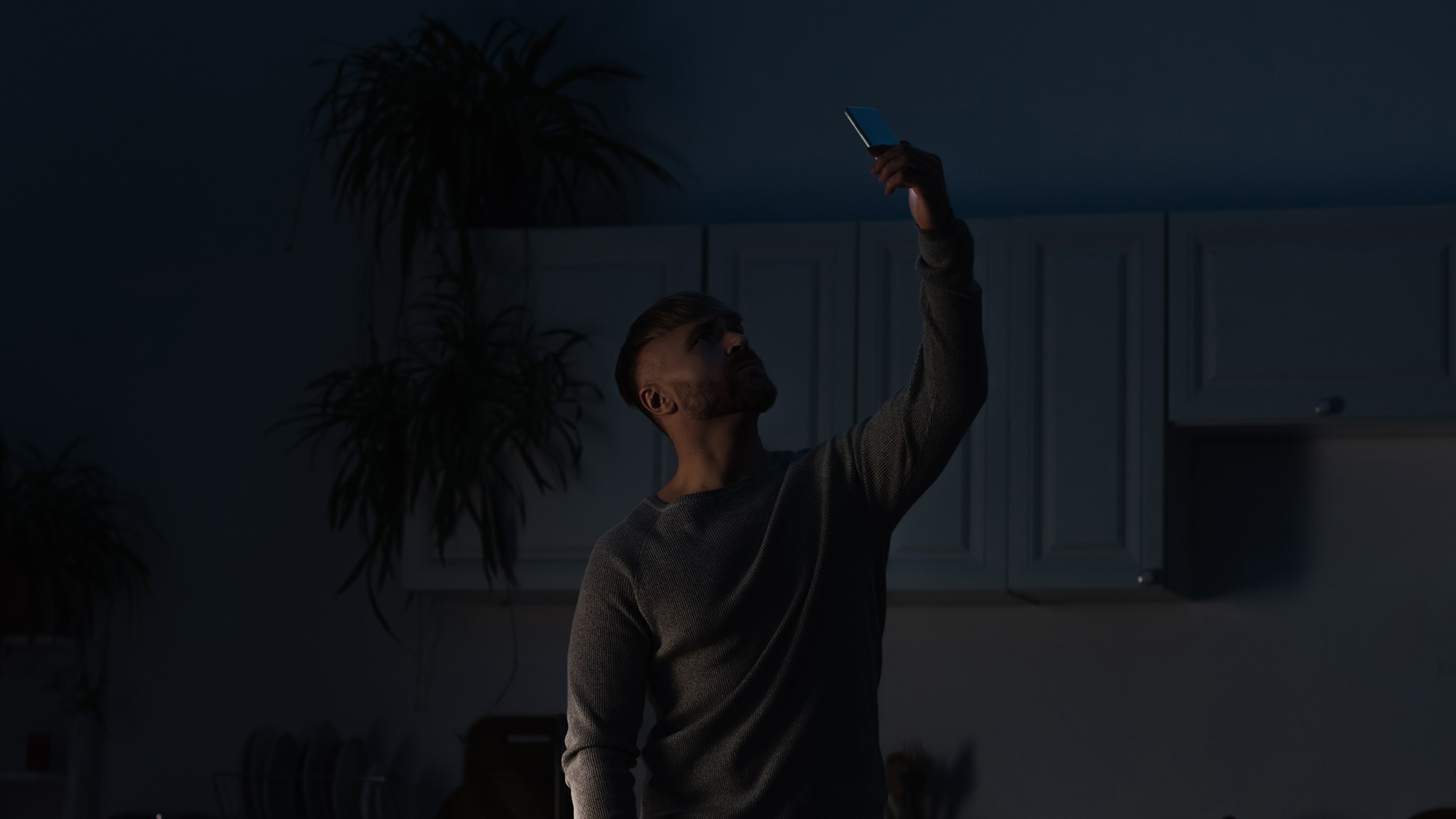 man holding smartphone in raised hand while searching for connection during energy blackout
