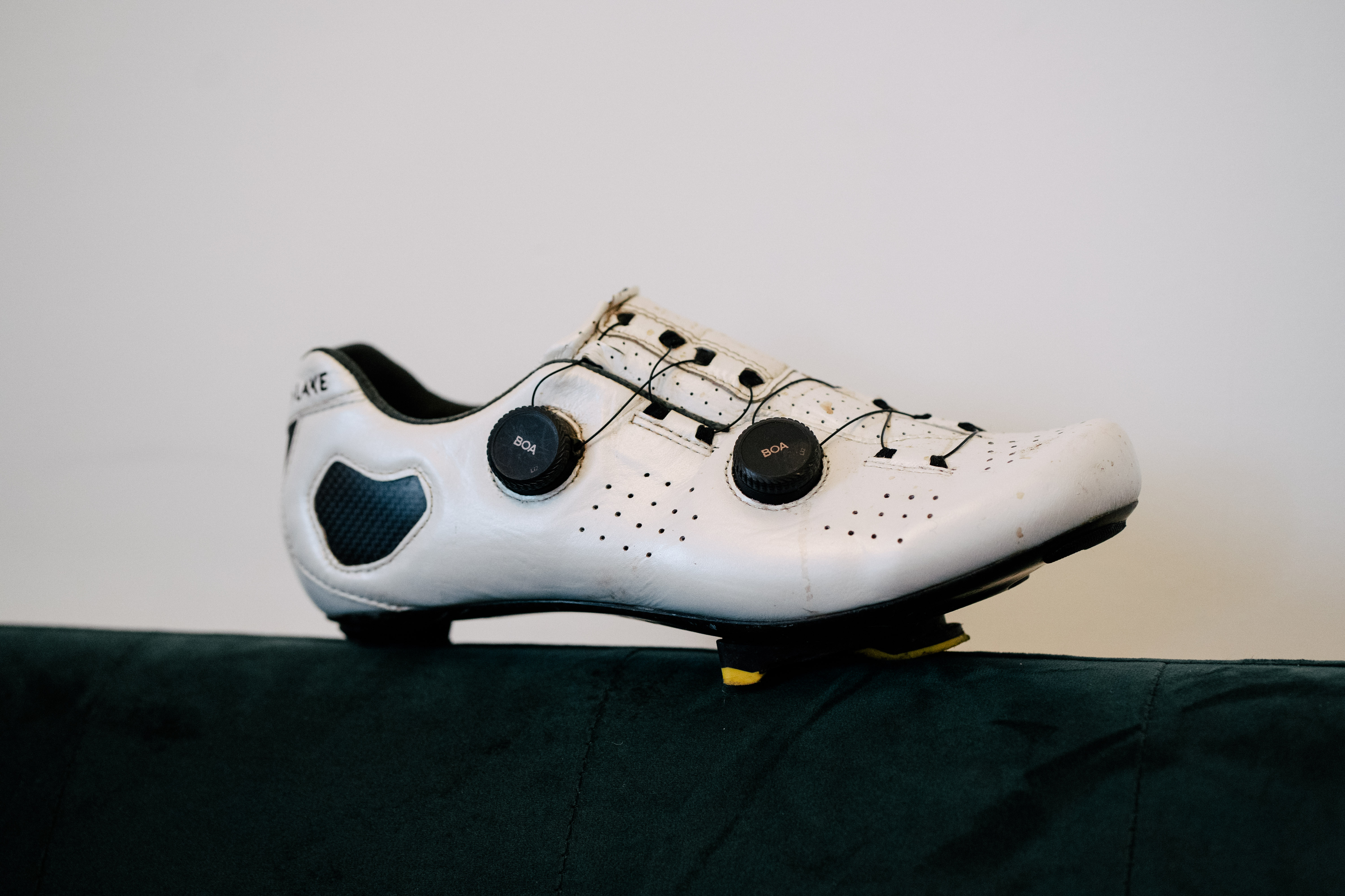 A white leather cycling shoe on a green sofa