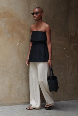 a photo of a woman wearing minimalist flat black sandals with white trousers and a strapless black top