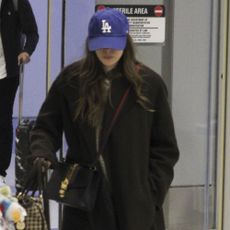 Elizabeth Olsen walks through the airport wearing black leather ankle boots, a black wool coat and a blue cap.
