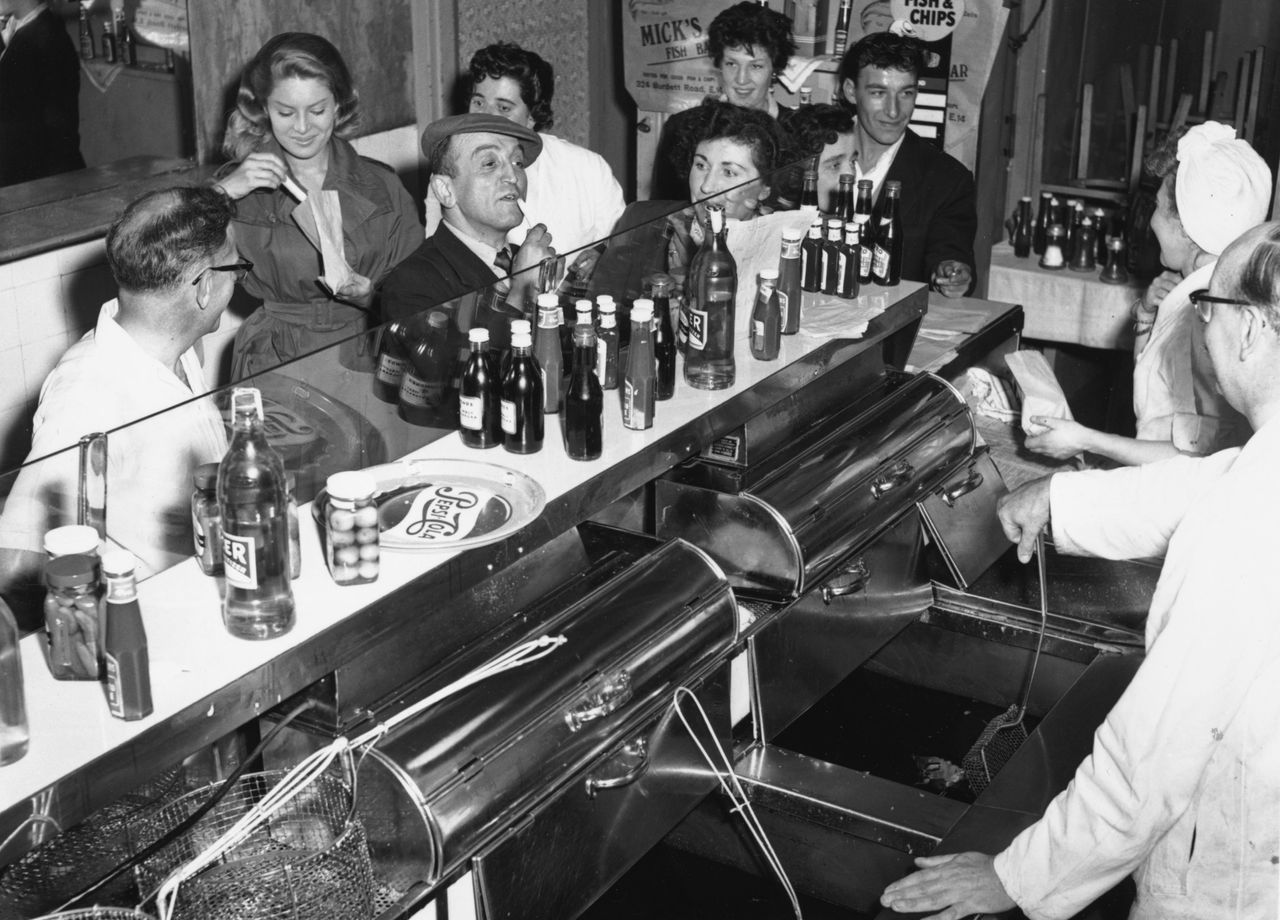 Black and white photo of people queuing up in a fish and chip shop