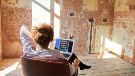 Woman sitting in an empty room looking at a laptop with paint colors and contemplating a renovation project