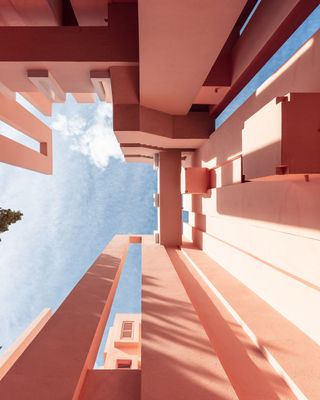 View from below of the tall pink exterior walls at La Muralla Roja by Ricardo Bofill in Calp, Spain. The sky is blue and cloudy