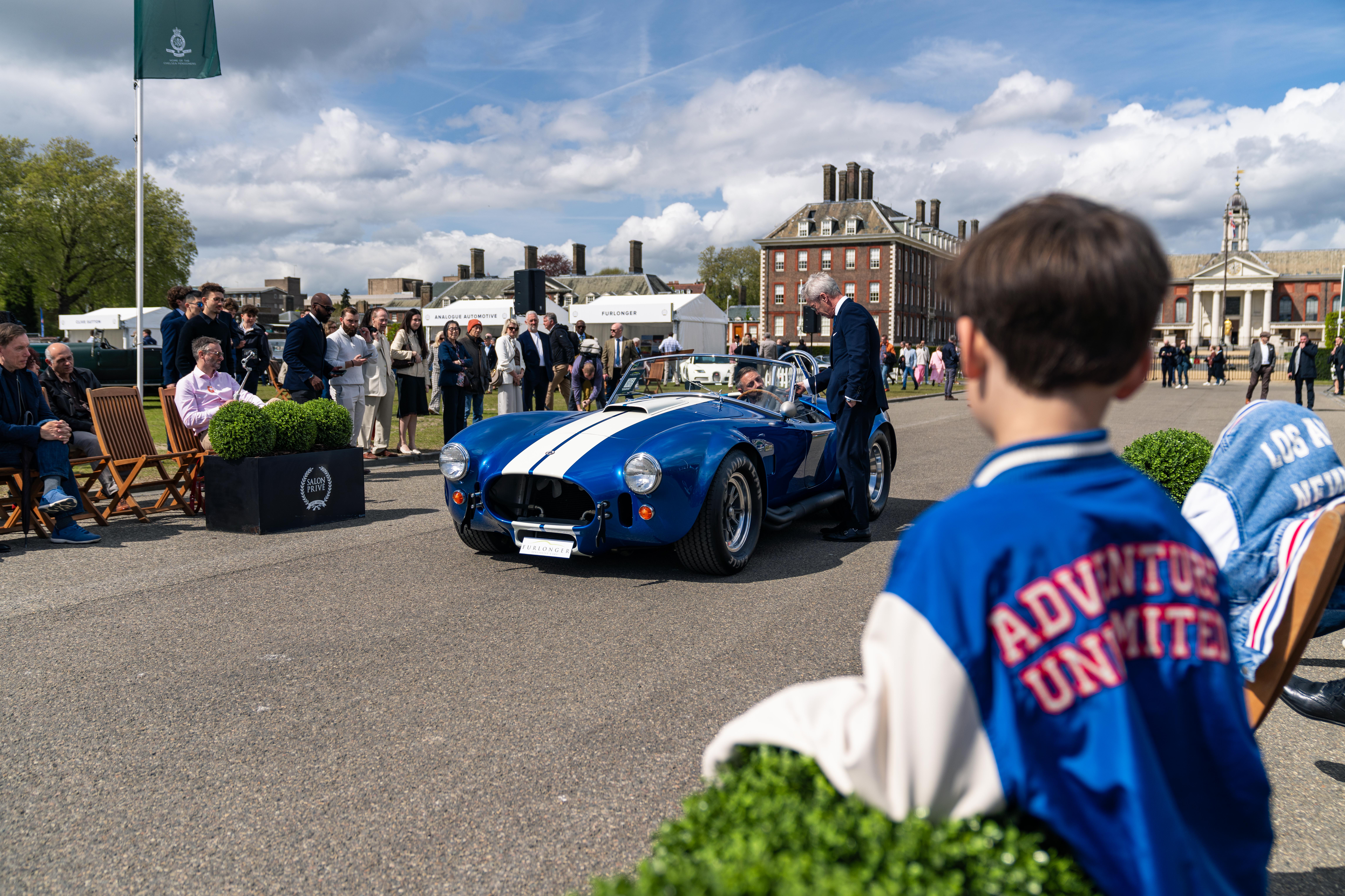 A young boy watches a blue ac cobra drive past