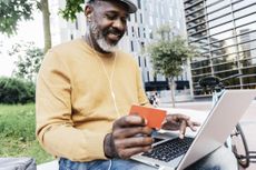 a dapper man holding his credit card while using his laptop