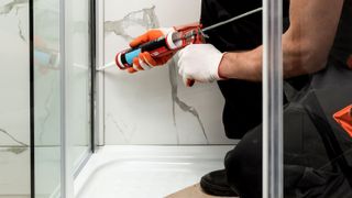 Peron using an orange caulking gun to seal a shower
