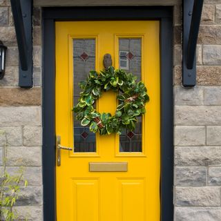 A yellow composite front door with a black frame decorated with a Christmas wreath